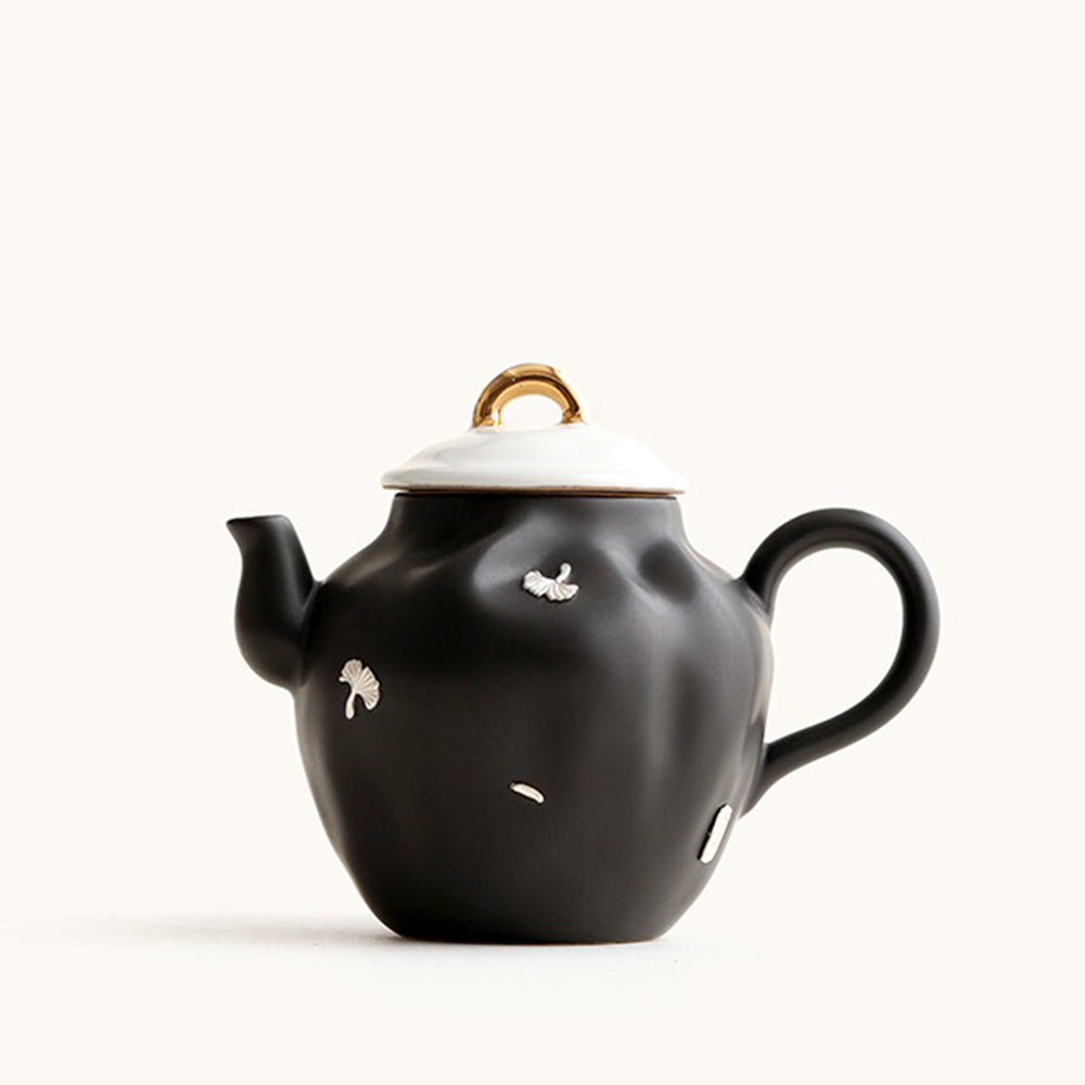 Elegant black ceramic Chinese teapot with ginkgo leaves, side view.