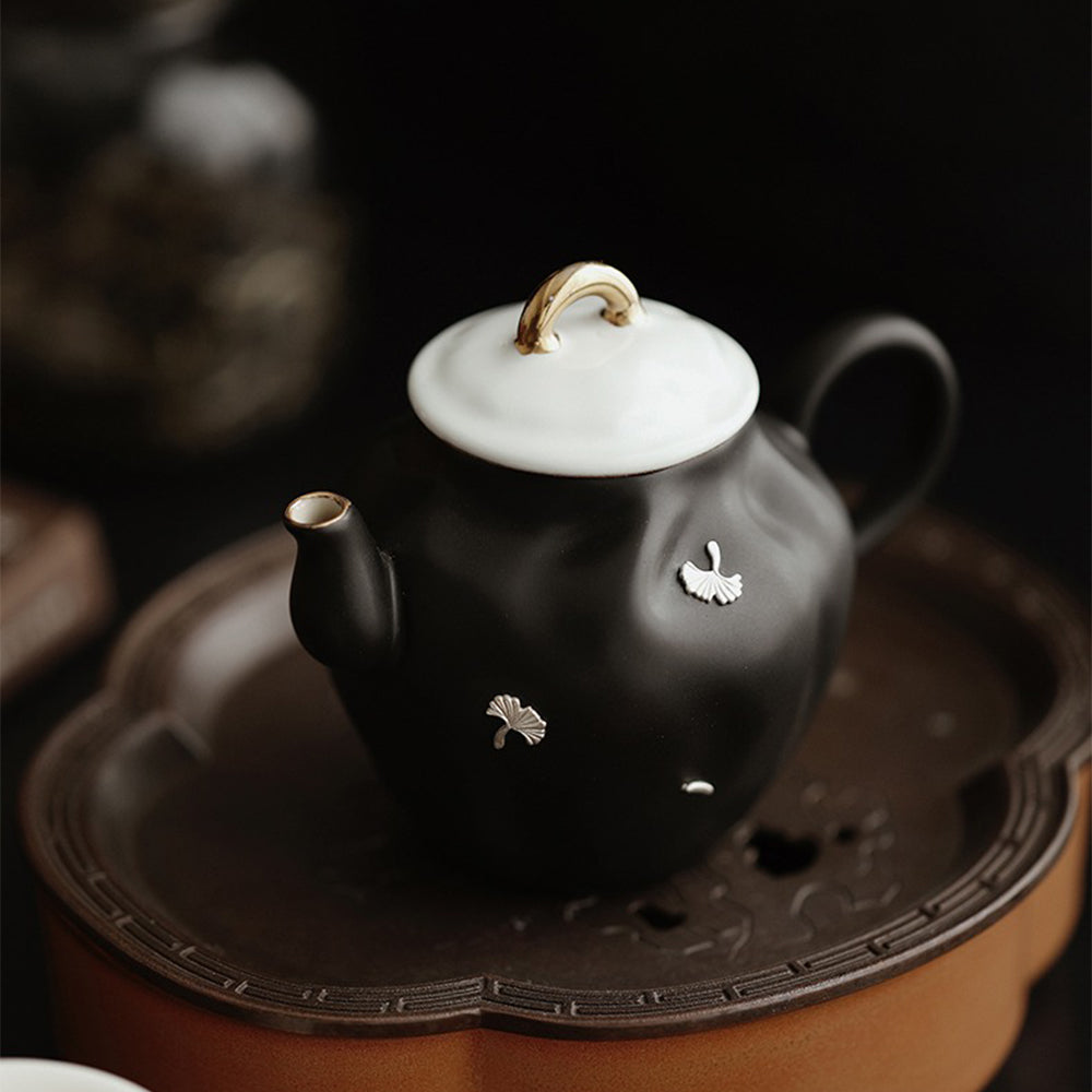 Black ceramic teapot with golden handle on an elegant table setting.
