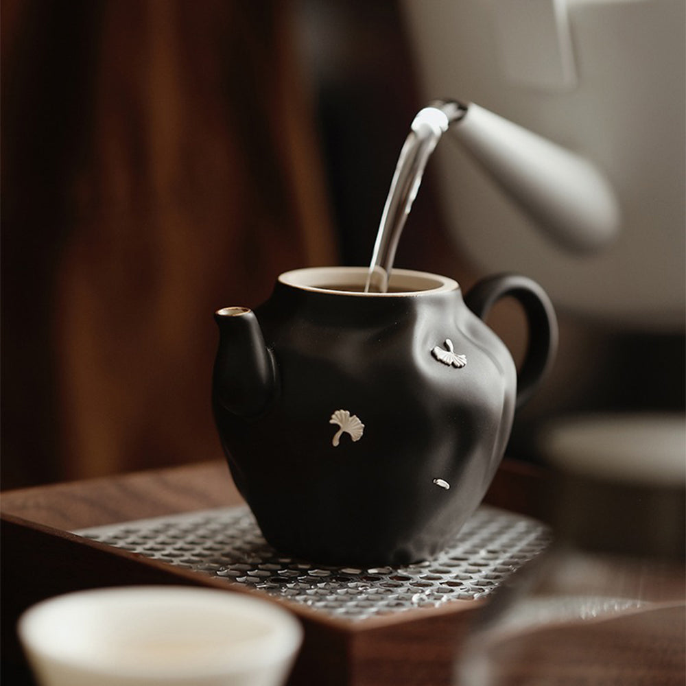 Elegant black ceramic Chinese teapot with ginkgo leaves, side view.