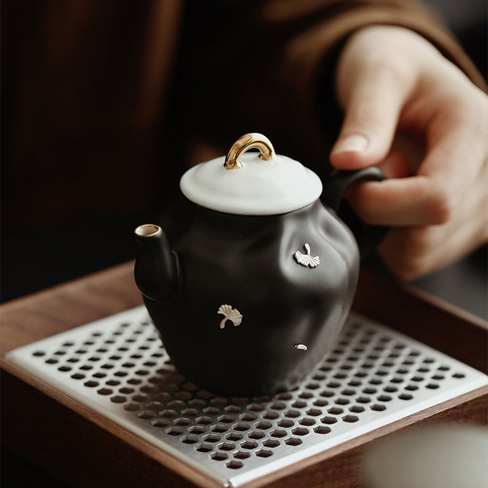 Black ceramic teapot with golden handle on an elegant table setting.