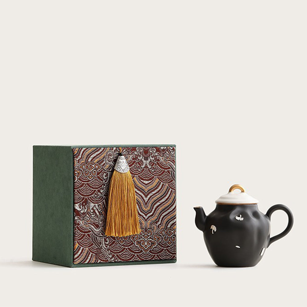Elegant black ceramic Chinese teapot with ginkgo leaves, side view.