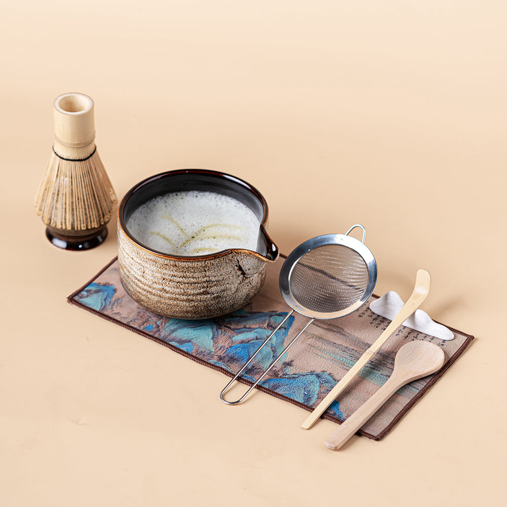 Hand holding bamboo whisk over ceramic tea set for matcha