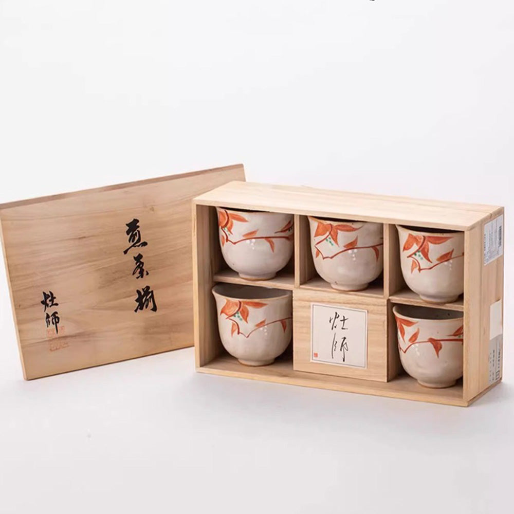 Close-up of handmade tea cups showcasing intricate red leaf patterns and mottled black glaze.