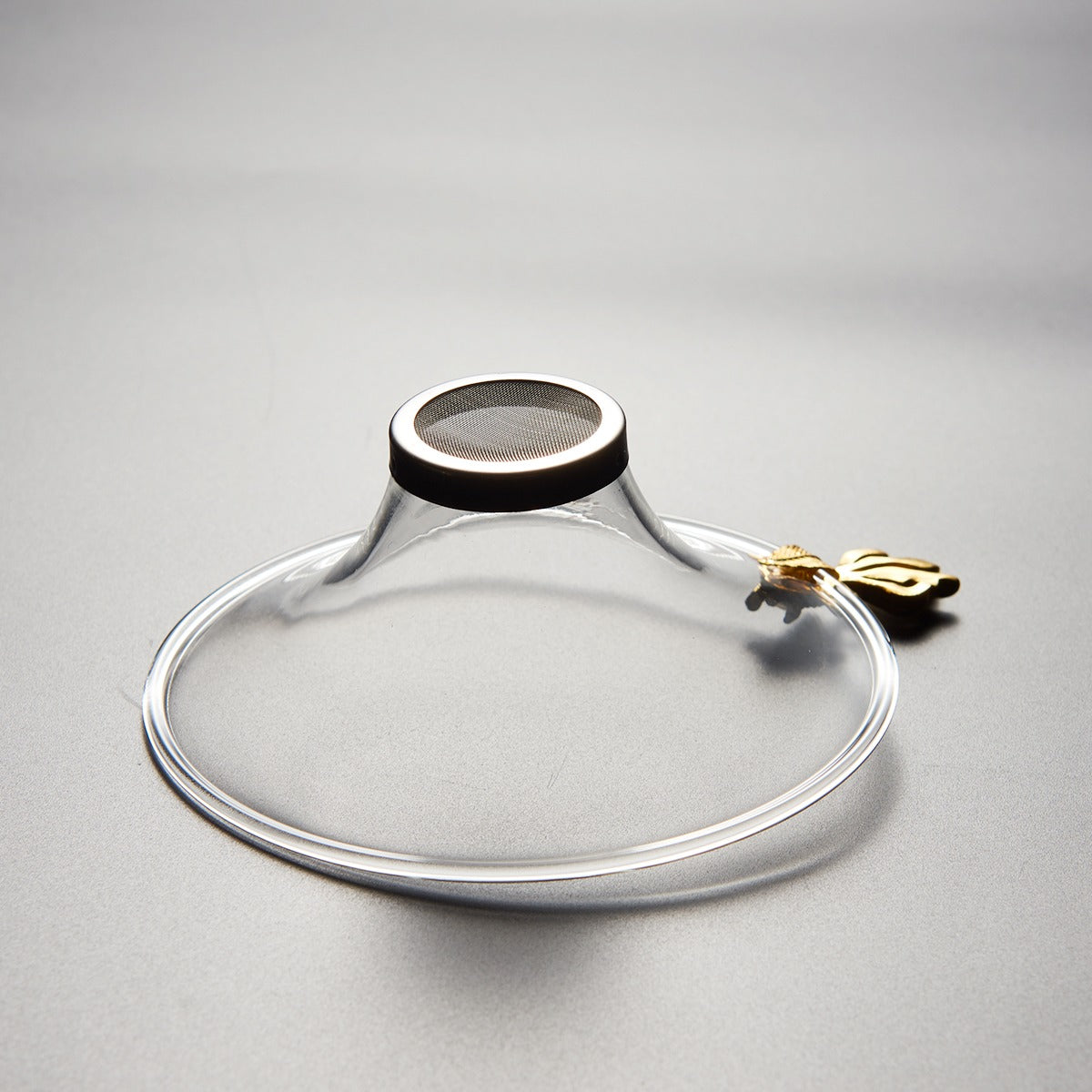 Top-down view of the goldfish-handle glass tea strainer placed over a fair cup for loose leaf pouring.