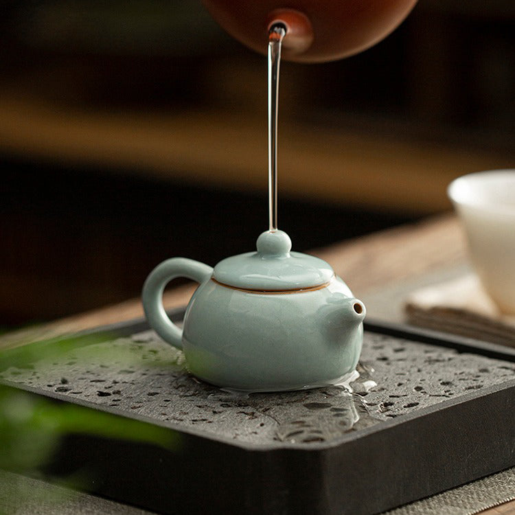 Hand holding the handmade teapot against natural light, showcasing glossy finish and compact size