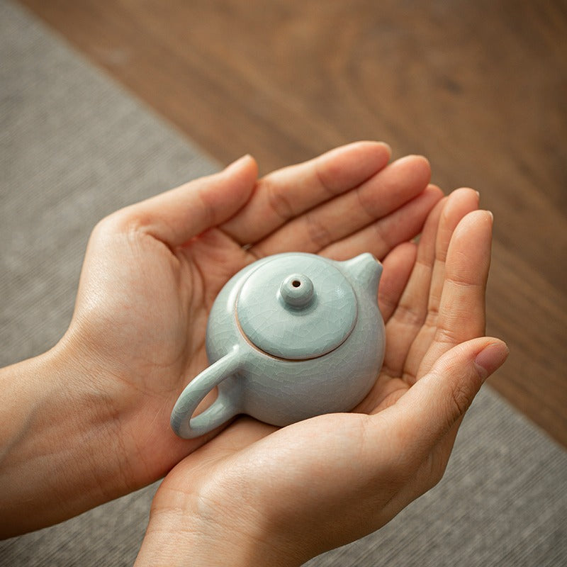 Hand holding the handmade teapot against natural light, showcasing glossy finish and compact size