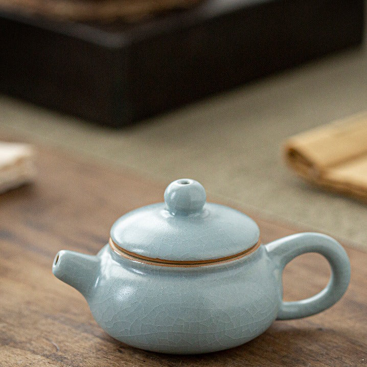 Hand holding the handmade teapot against natural light, showcasing glossy finish and compact size