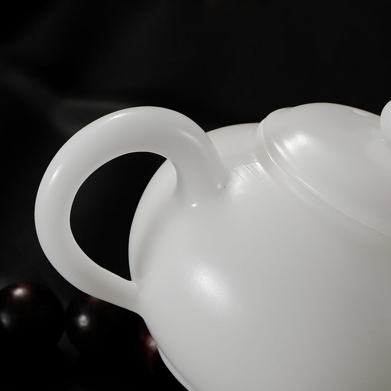 Side profile of white teapot displayed on bamboo tray for tea ceremony setting.