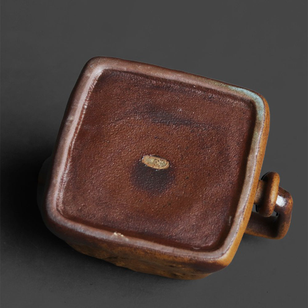 Side view of the artistic ceramic teapot highlighting its square lid knob and cultural motifs