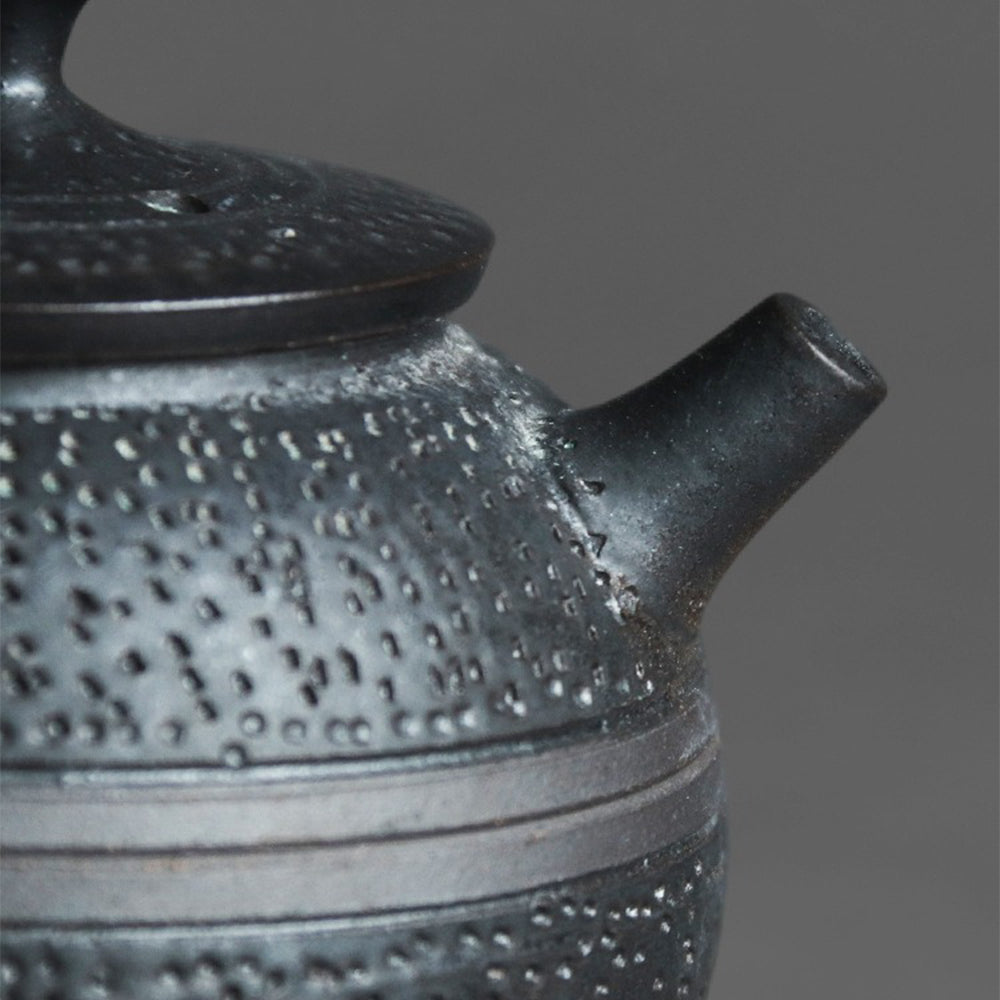 Black ceramic teapot with a focus on the round-ear handle for comfortable pouring