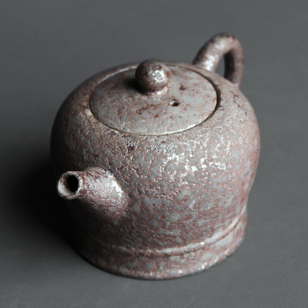 Pouring tea from rustic clay teapot with rust glaze