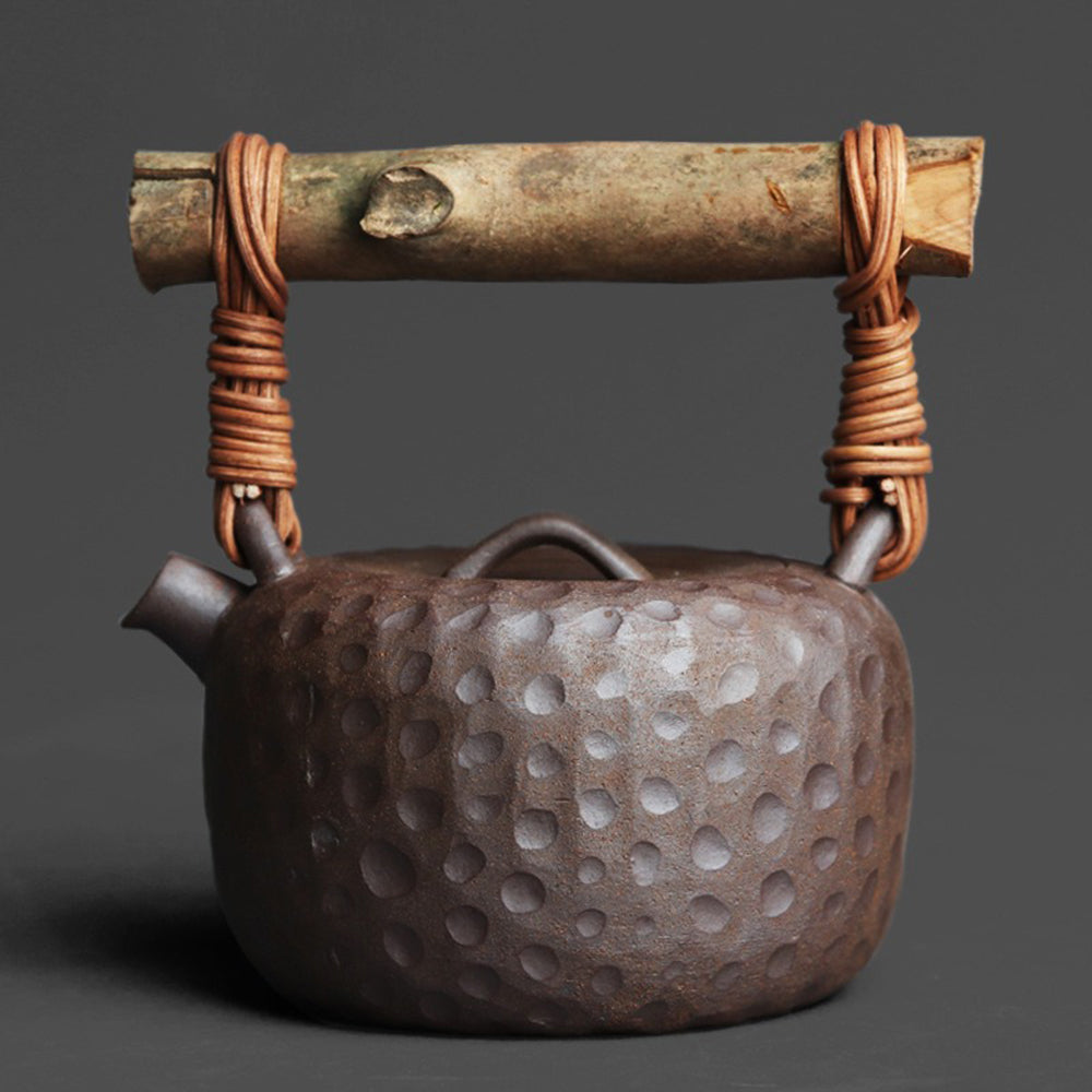 Artisan Japanese clay teapot with textured hammered surface and rattan handle, front view