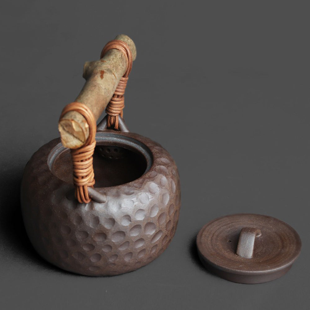 Artisan Japanese clay teapot with textured hammered surface and rattan handle, front view