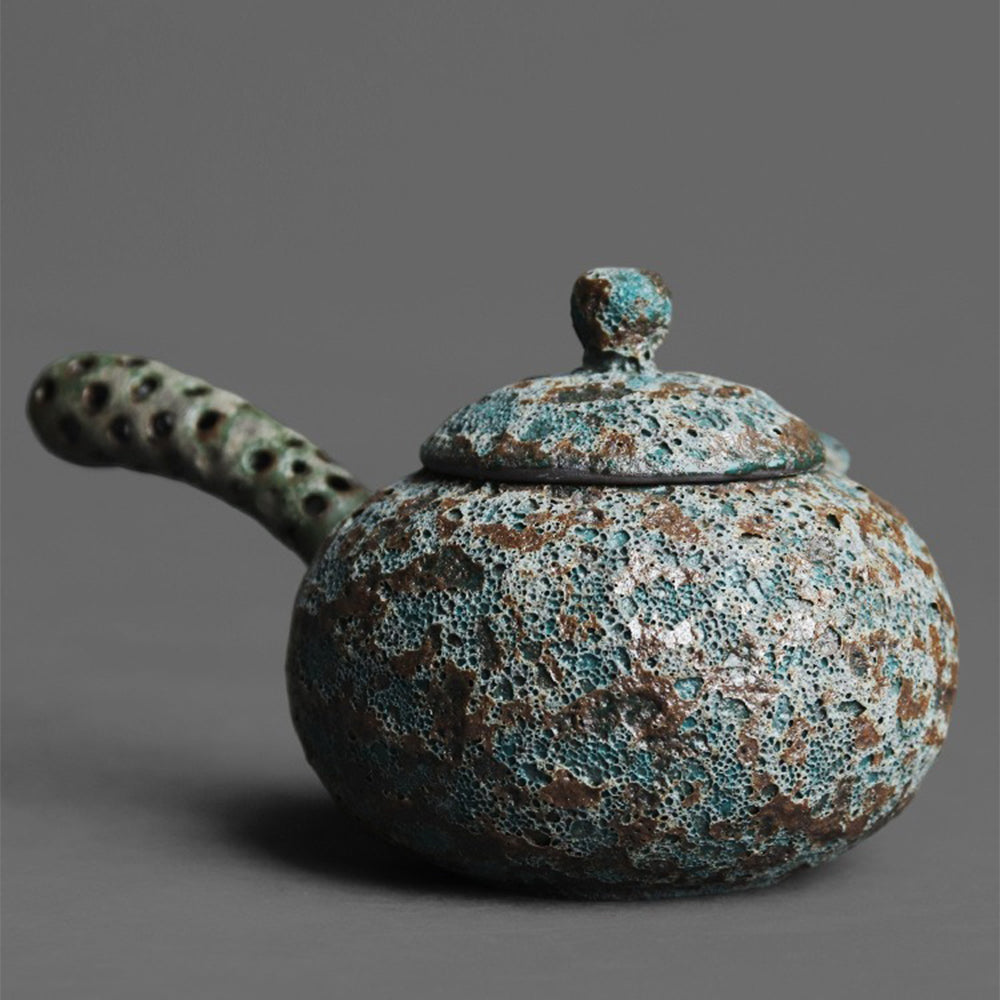 Wormhole Bronze Kyusu Teapot displayed with loose tea leaves and a tea cup.