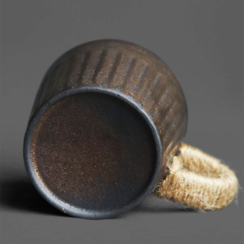 Close-up of black gold kiln coarse pottery tea cup with detailed texture and saucer