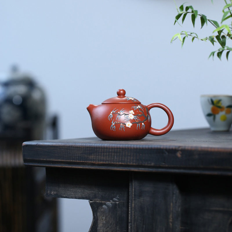 Traditional Chinese teapot with peach blossom patterns displayed on a tea table.
