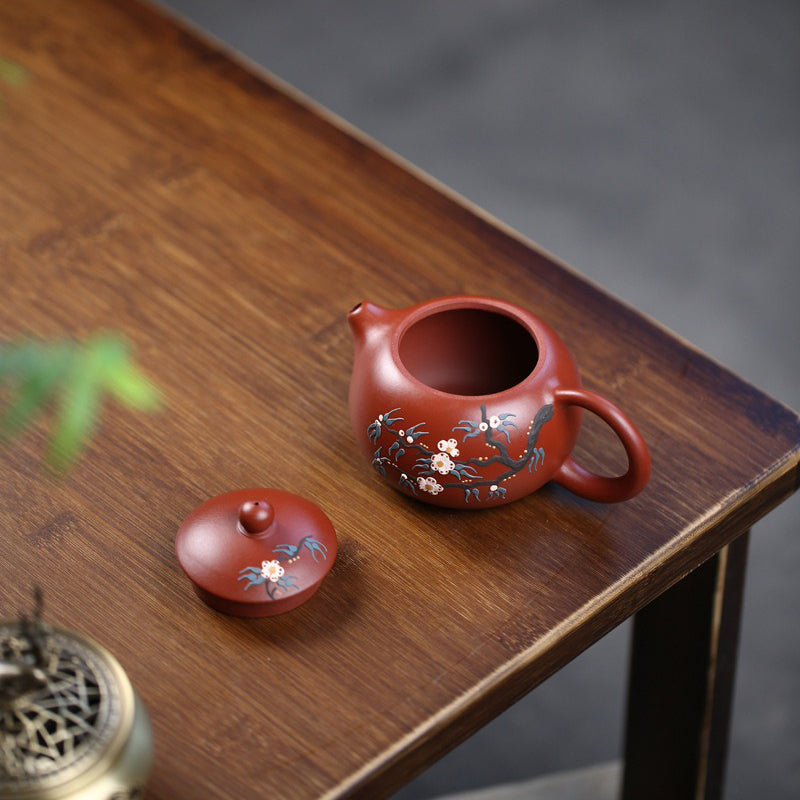 Traditional Chinese teapot with peach blossom patterns displayed on a tea table.