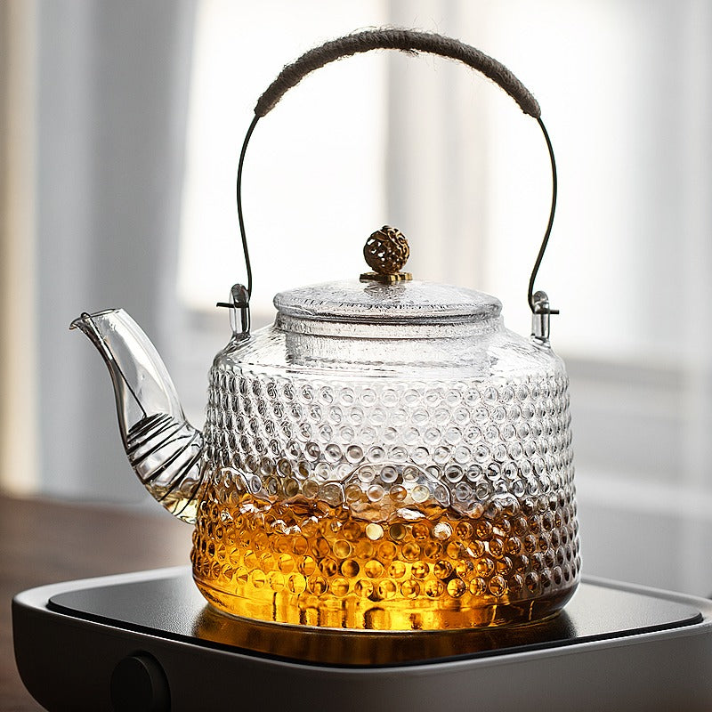 Rivet-Style Heat-Resistant Glass Teapot on a teapot warmer, maintaining heat.