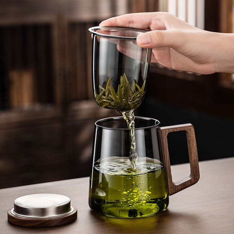 Hand holding a glass tea cup with infuser, showing its elegant design
