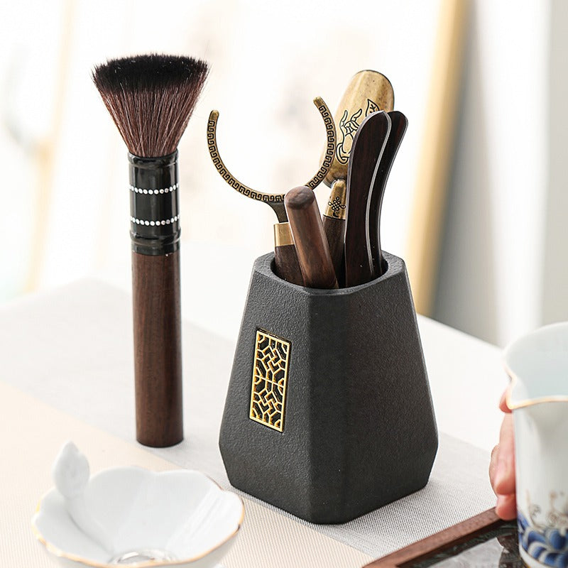 Ebony tea utensils in use, with hot tea being poured into a cup from the brewing pot.