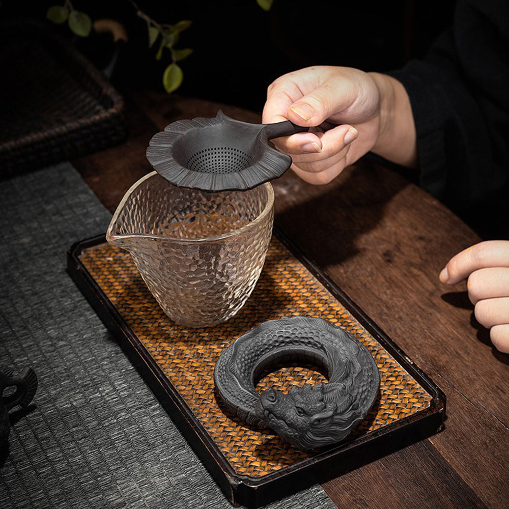 Handmade tea strainer with dragon design surrounded by tea accessories, highlighting its decorative appeal.