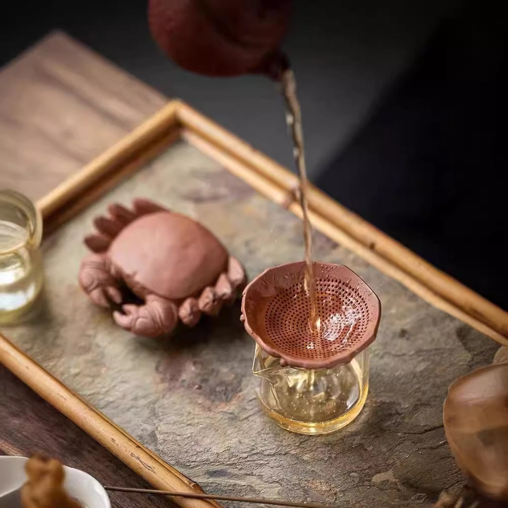 Purple clay crab tea pet with detachable shell, shown filtering tea in a traditional setting