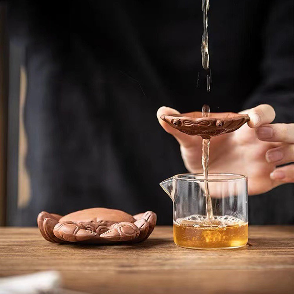 Purple clay crab tea pet with detachable shell, shown filtering tea in a traditional setting