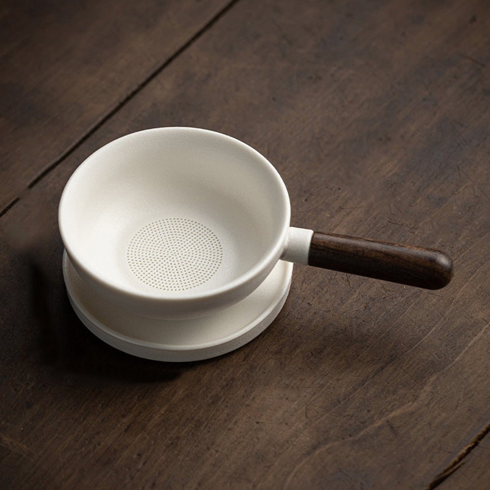 Elegant ceramic tea strainer with wooden handle on a table, showcasing its beautiful design.