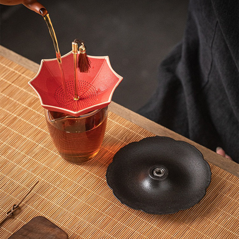 Close-up of the ceramic umbrella tea strainer with loose tea leaves, highlighting its filter holes.