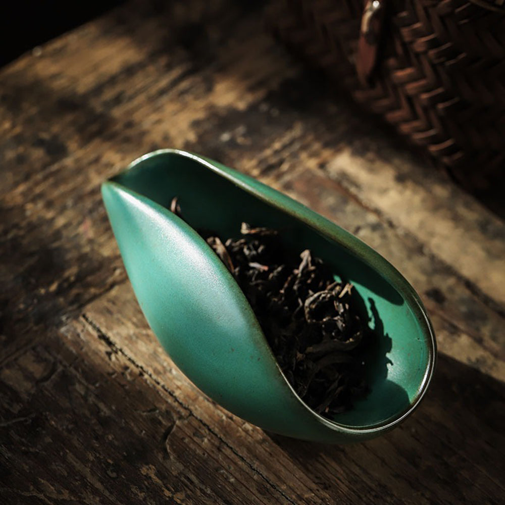 Close-up of the coarse pottery tea holder with dark green glaze and black mineral spots, showcasing craftsmanship