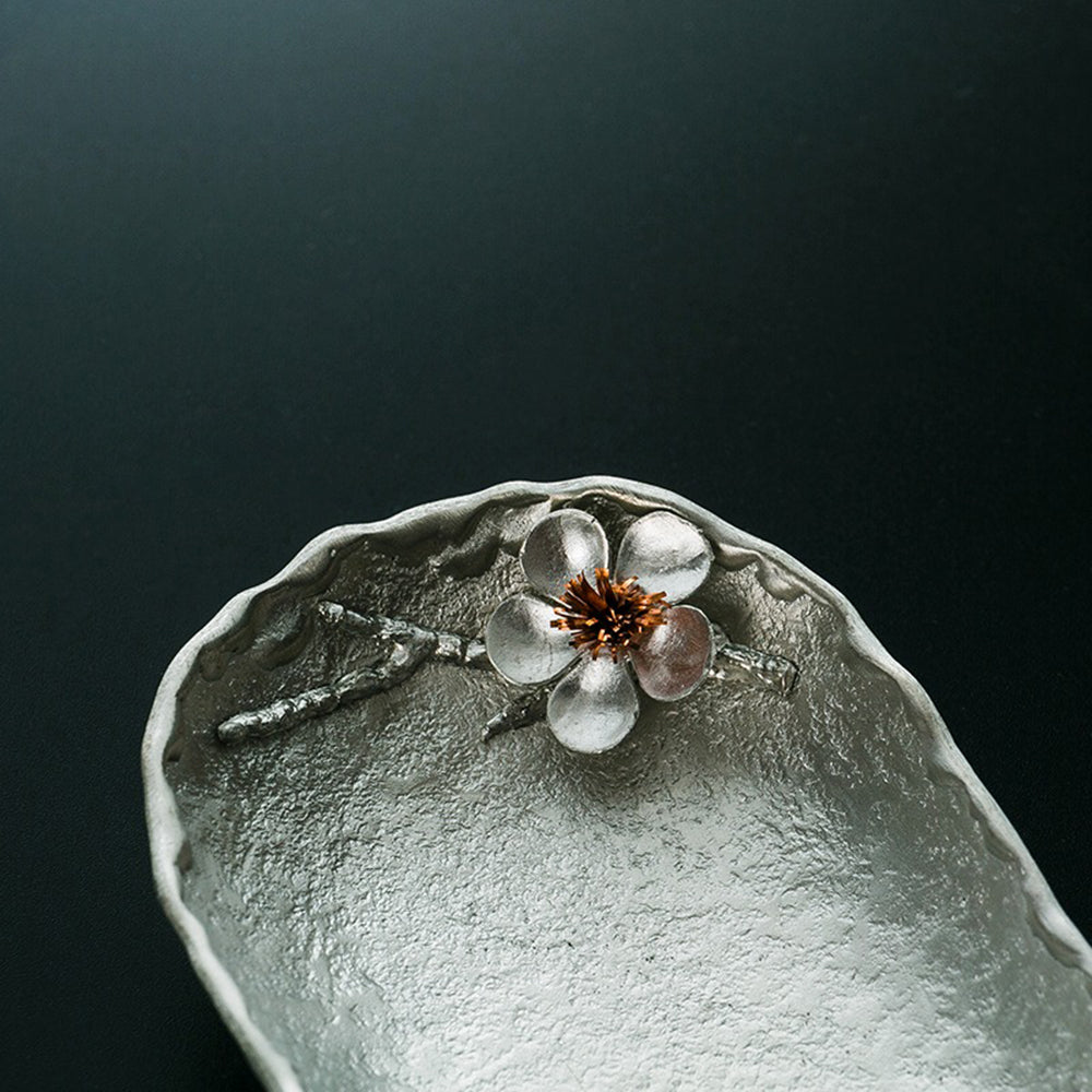 Elegant tin tea holder with spoon and stand, showcasing plum blossom design.