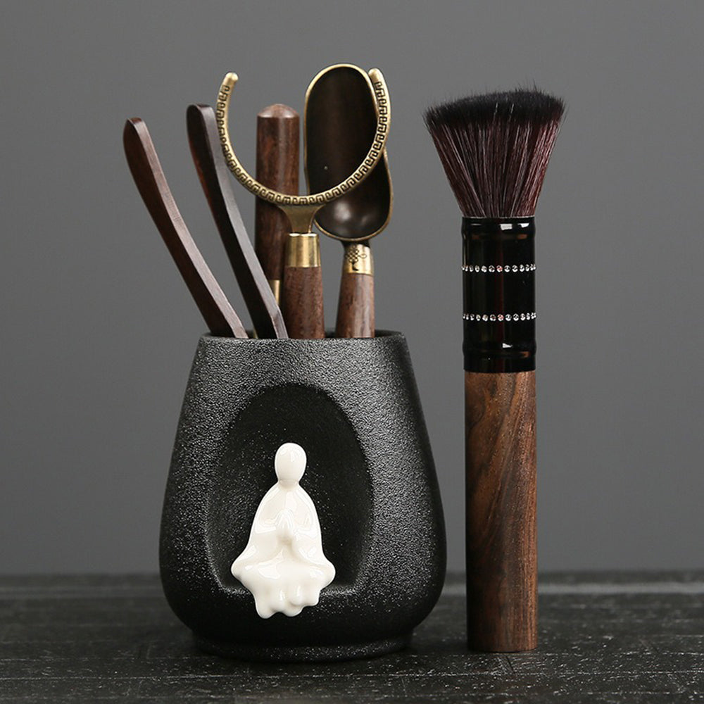 Close-up of Zen ebony tea utensils set with black pottery holder and ceramic monk decoration