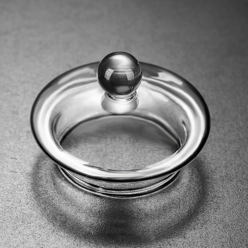 Hand holding a clear glass teapot with blooming tea inside, perfect for tea enthusiasts