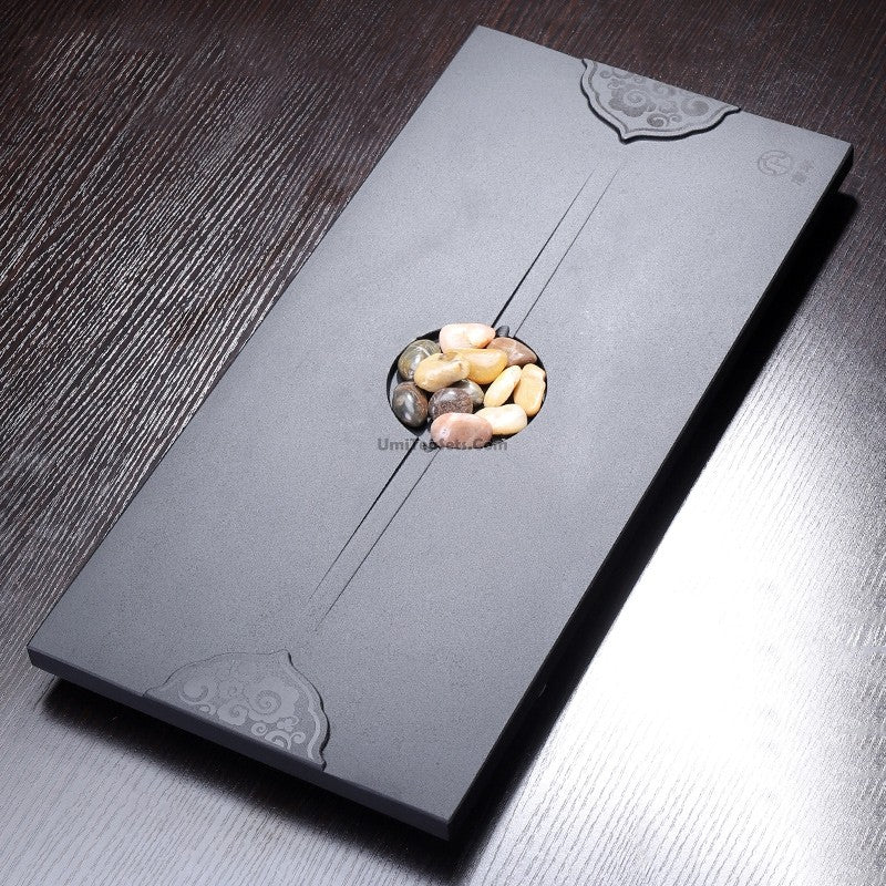 Close-up of black stone gongfu tea tray with cobblestone texture, showing drainage pipe